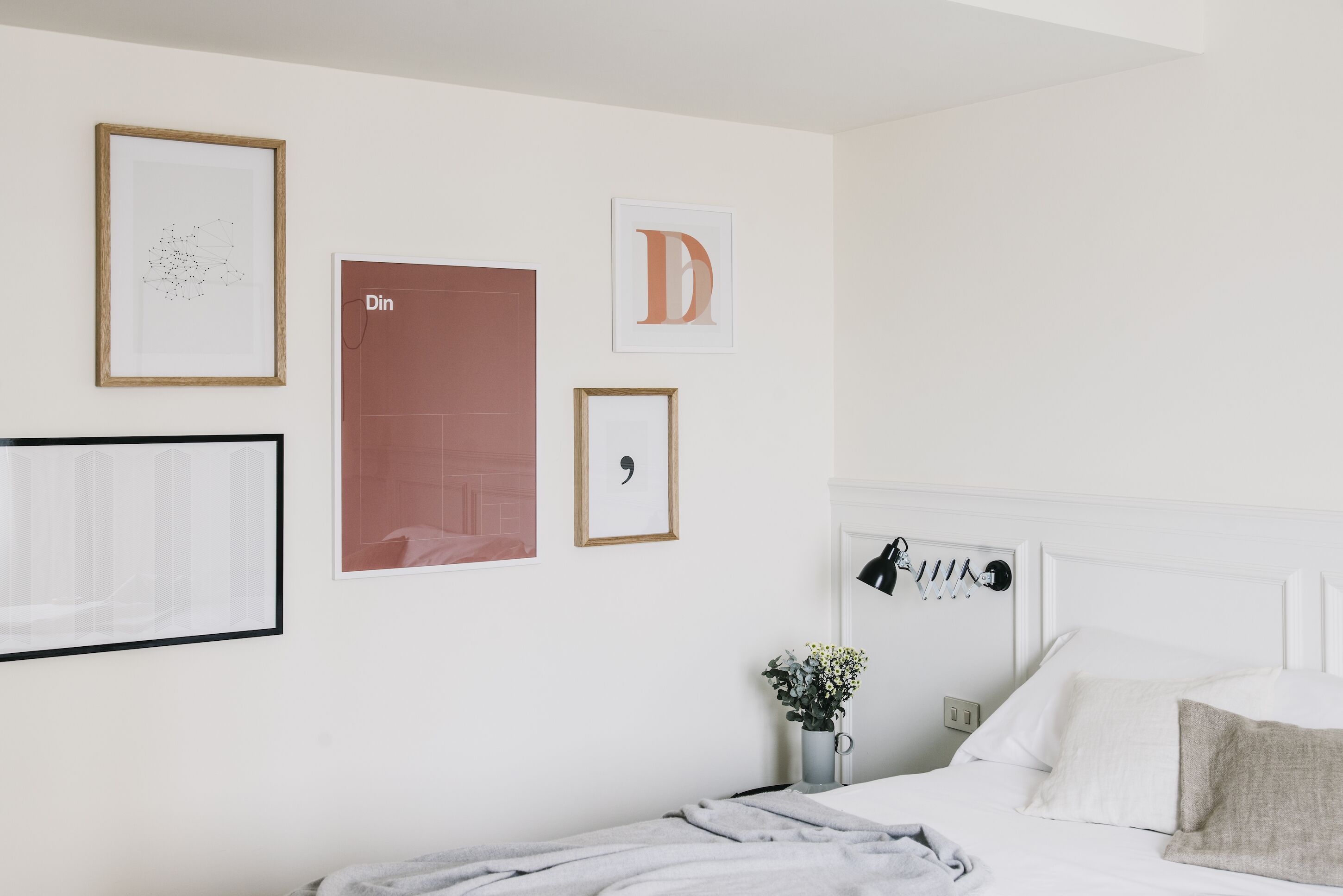 Un dormitorio con una cama, una mesita de noche con lámpara, y decoración en la pared que incluye letras y un cuadro enmarcados.