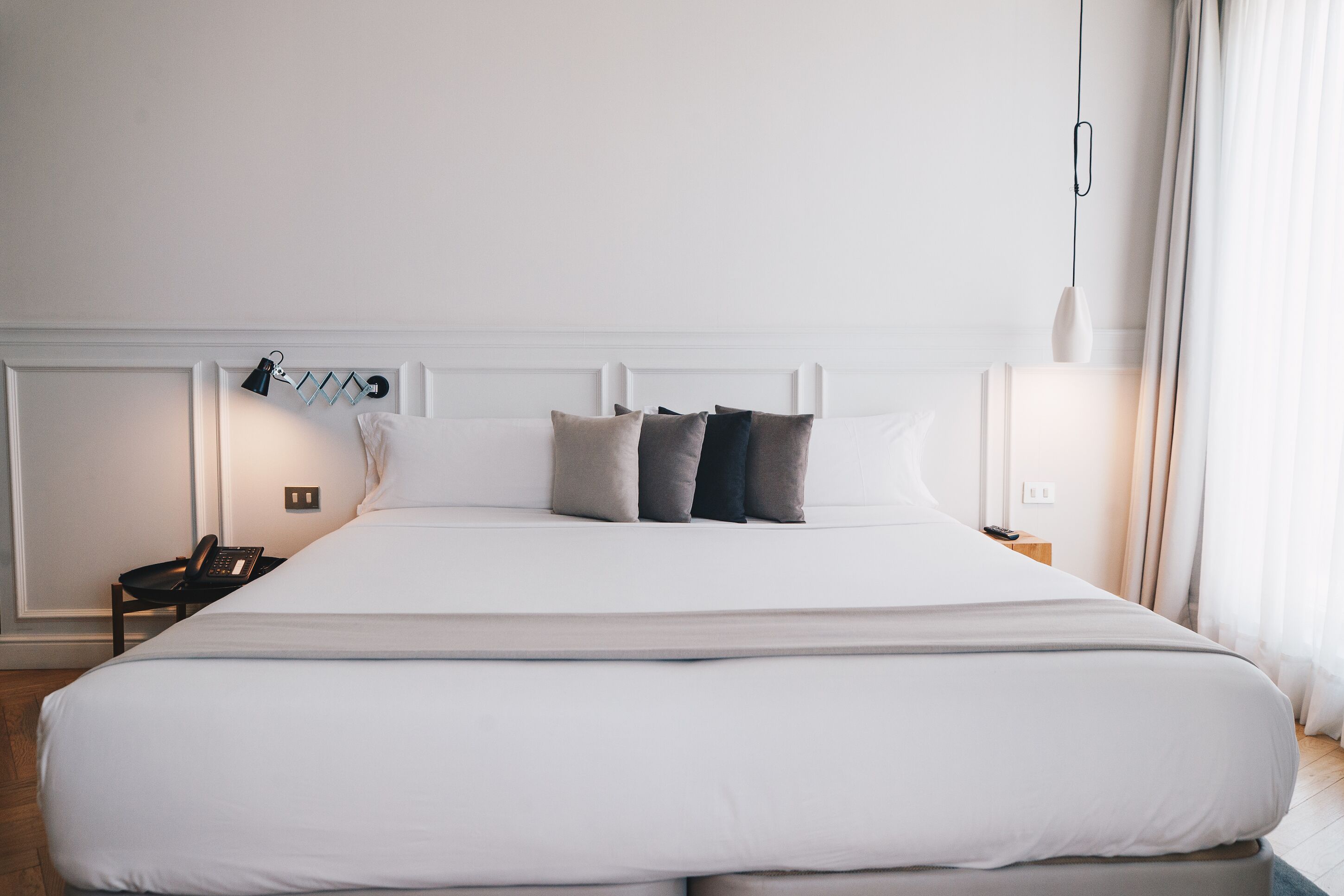 Una cama grande con ropa de cama blanca, una lámpara de noche y un teléfono en la mesita.