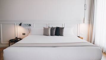 Una cama grande con ropa de cama blanca, una lámpara de noche y un teléfono en la mesita.