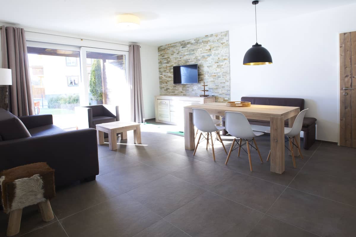 A modern living room with a sofa, a small wooden stool, and a dining area with a table and chairs.