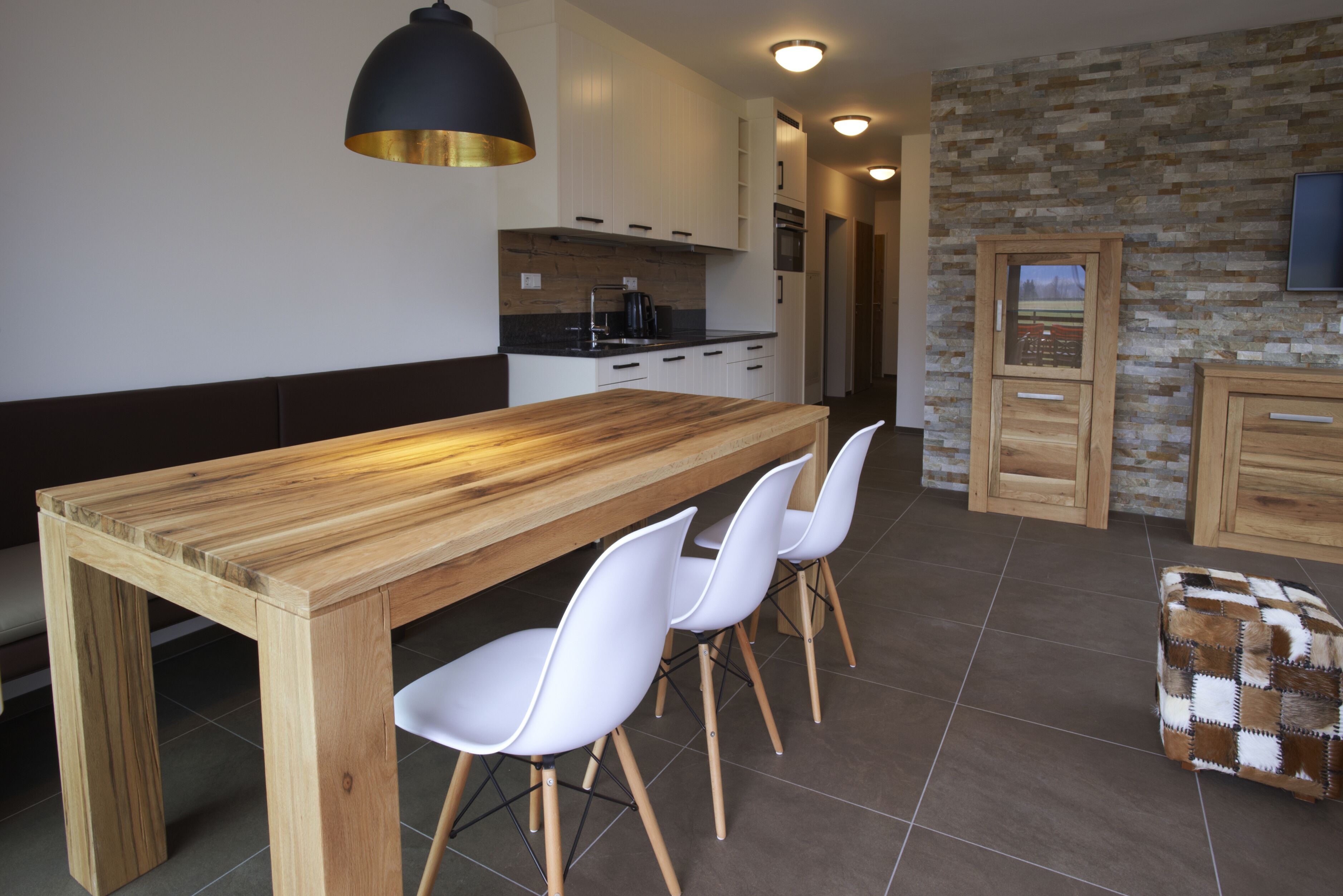 A modern kitchen with a wooden table, white chairs, and a stone wall.