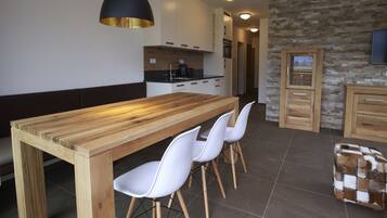 A modern kitchen with a wooden table, white chairs, and a stone wall.