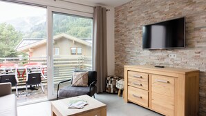 Een moderne woonkamer met een grote televisie, houten meubels en een schuifdeur naar een buitenruimte met een tafel en stoelen.