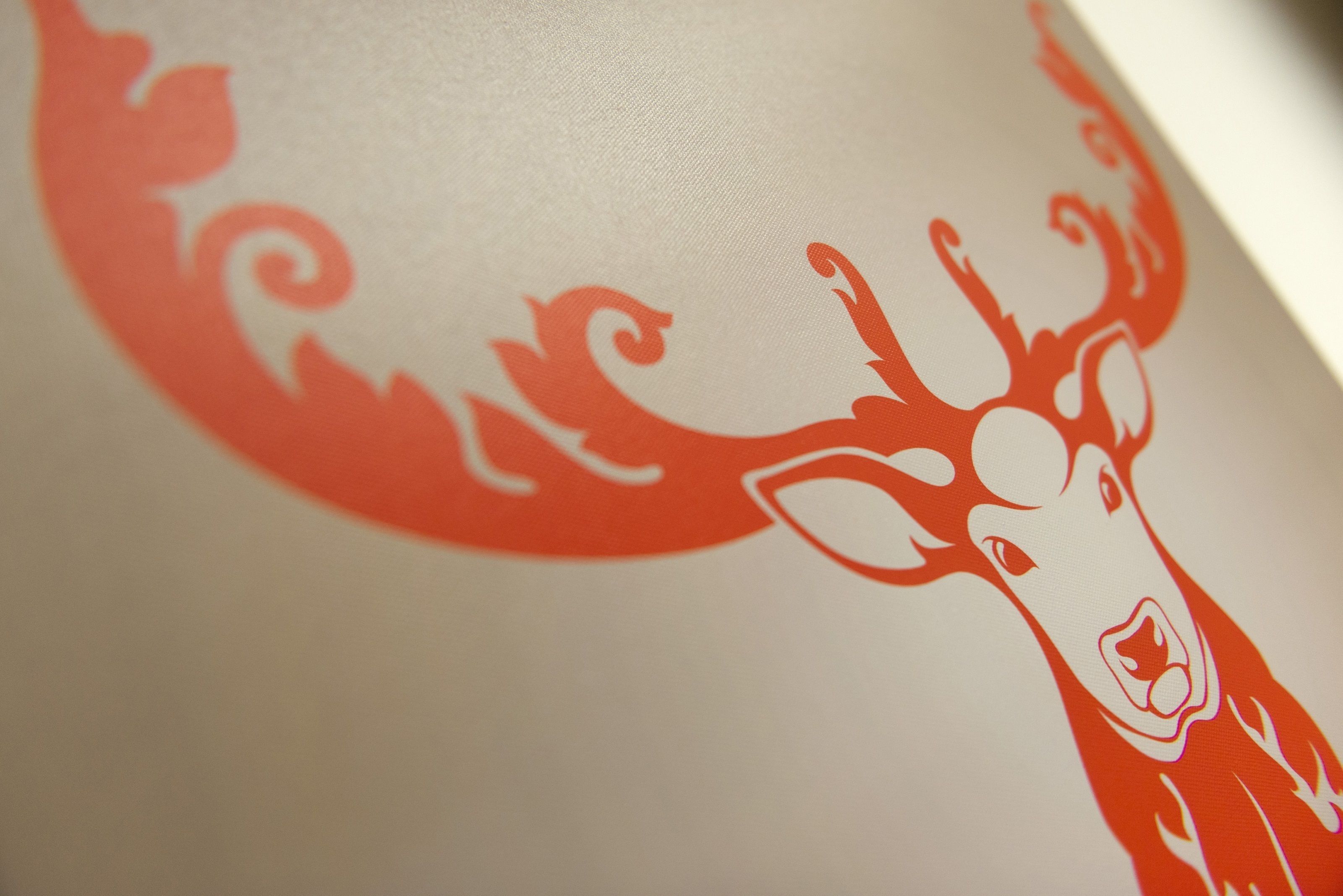 Close-up van een logo van een hertenkop in rood tegen een witte achtergrond.