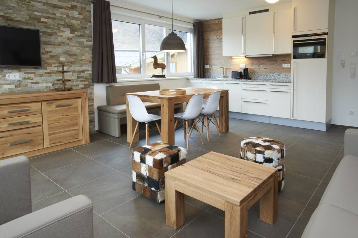 A modern kitchen with white cabinets, a dining table with chairs, and a TV mounted on the wall.