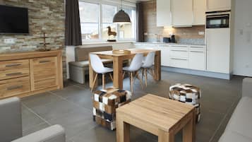 A modern kitchen with white cabinets, a dining table with chairs, and a TV mounted on the wall.