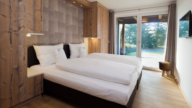 Een slaapkamer met een groot bed, houten lambrisering, een schuifdeur naar een balkon en een tv aan de muur.