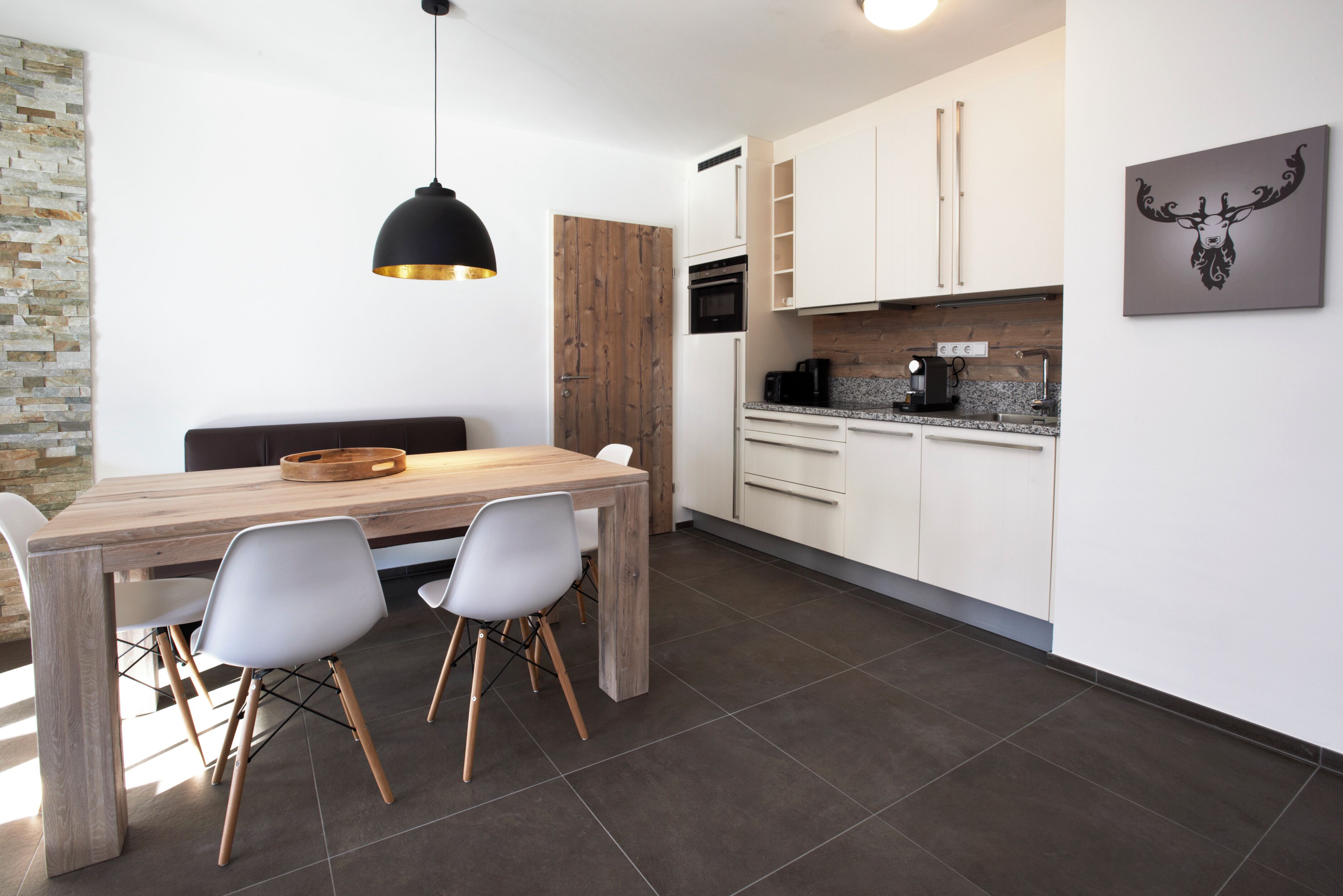 Een moderne keuken met een houten eettafel, witte stoelen en een zwarte hanglamp.