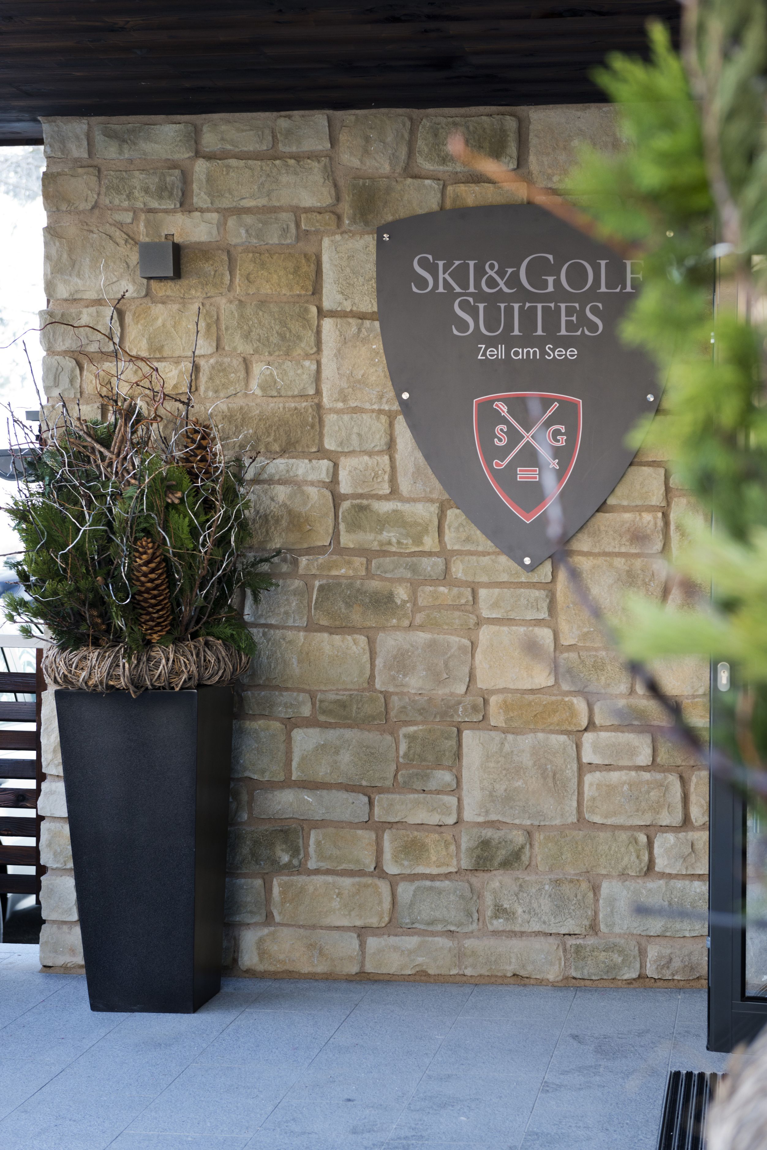 Eine Steinmauer mit einem Schild für "Ski & Golf Suites" und einem Blumentopf mit Kiefernzapfen.