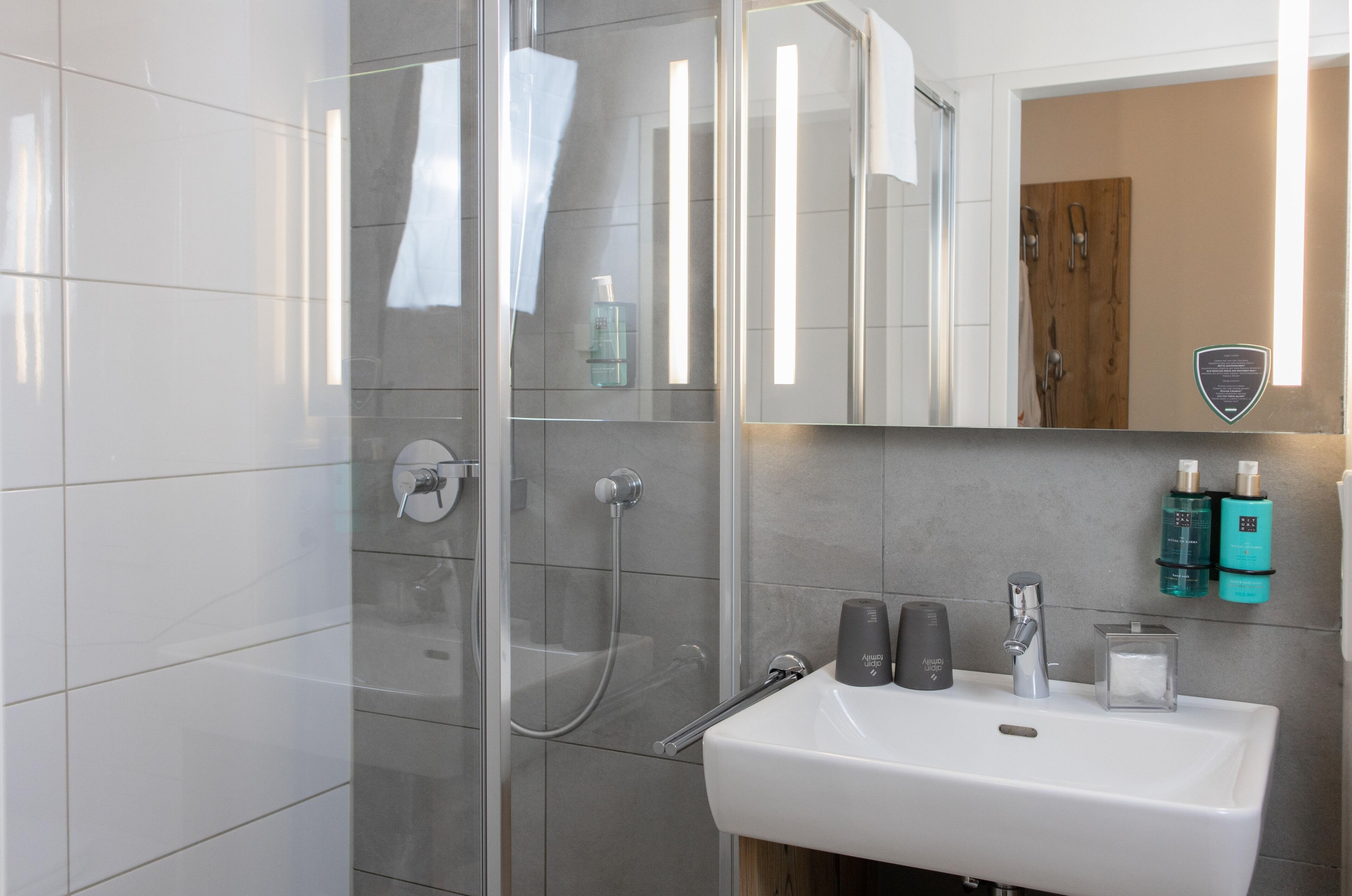 A modern bathroom with a glass shower enclosure, a white sink, and toiletries on the wall.