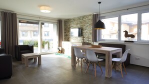 Een moderne woonkamer met een eetgedeelte, grote ramen, een flatscreen televisie en een stenen muur.