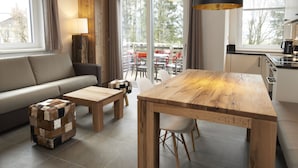 Een moderne woonkamer met een bank, een houten salontafel en een eettafel met stoelen.