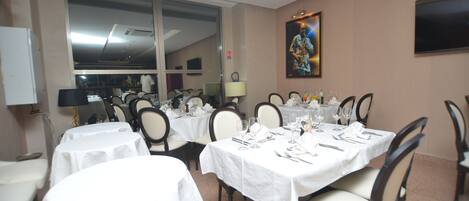 A dining area with multiple tables set for service, chairs, and a large window providing a view of the interior.