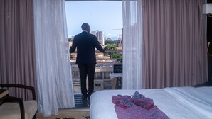 A hotel room with a bed, a chair, and a view of the city through sheer curtains. - Hôtel Fleur de Lys Plateau (Dakar)