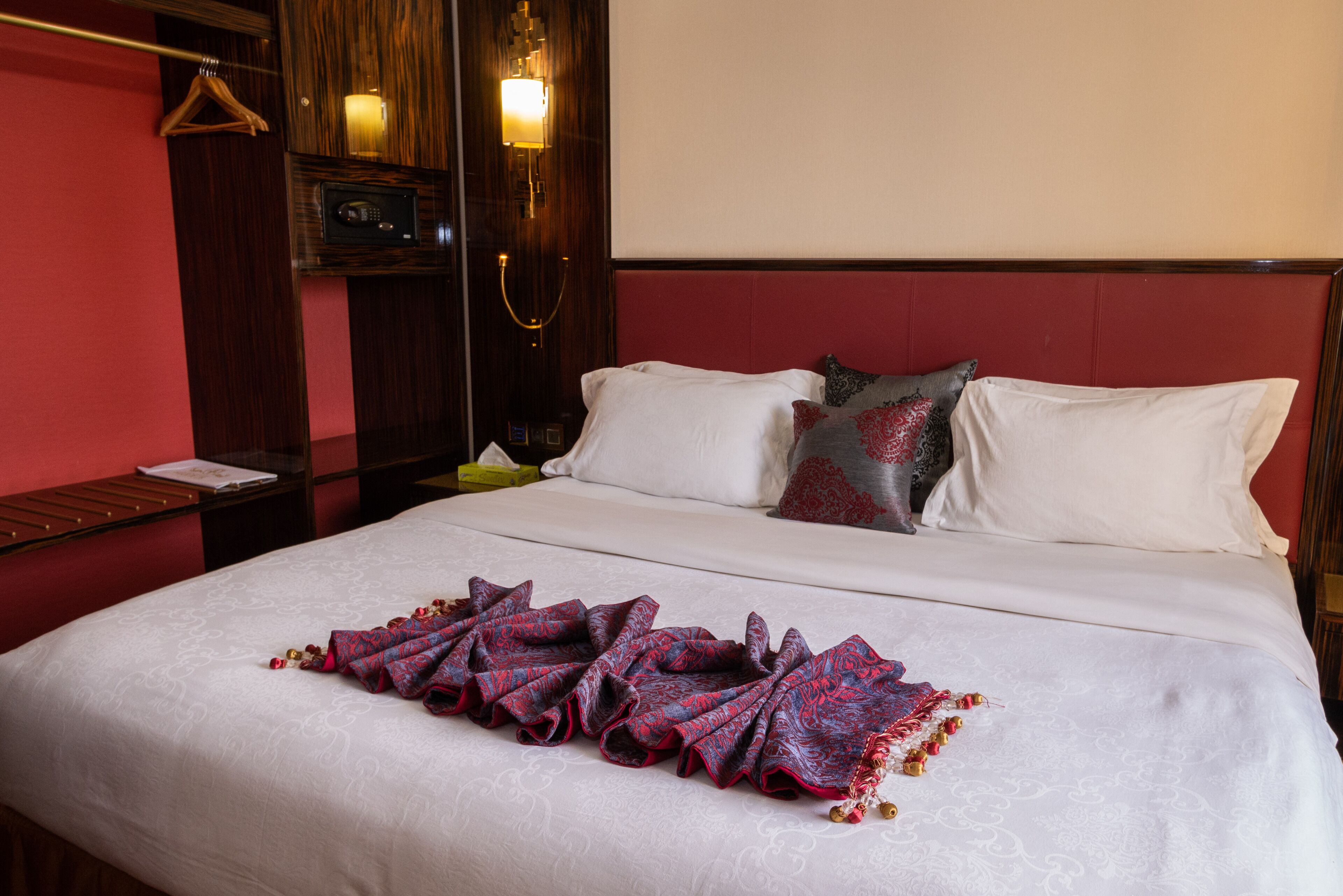 Cama bem arrumada com manta estampada, mesa de cabeceira com abajur e cabeceira de madeira.