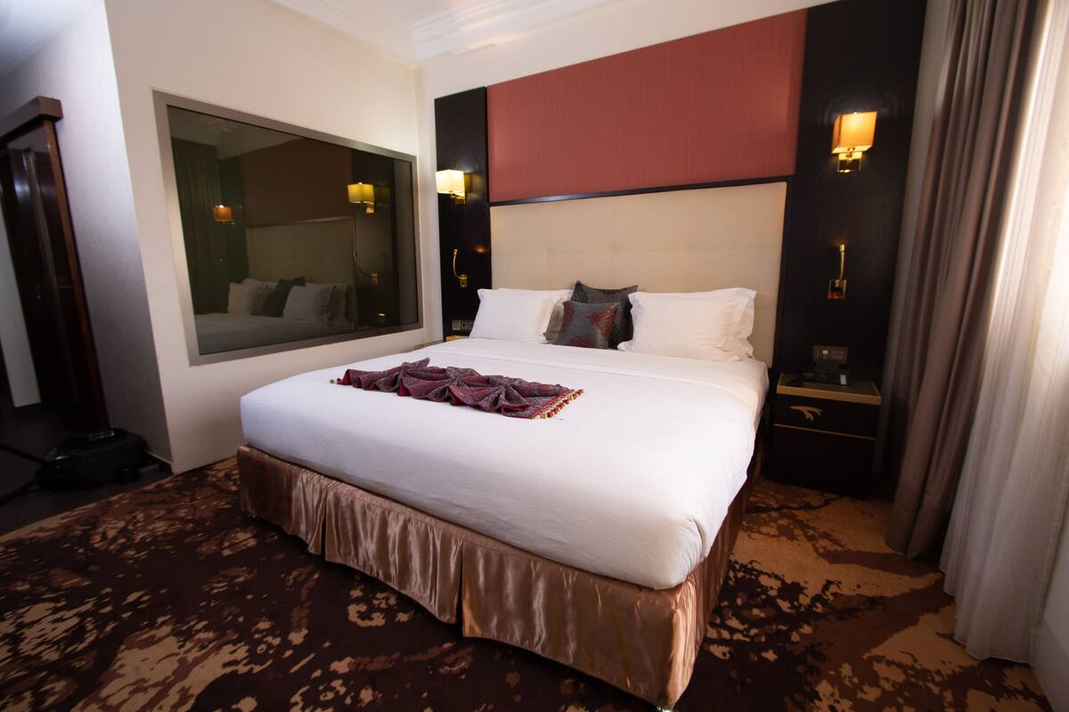 Une chambre d’hôtel avec un grand lit, un miroir, une table de chevet et une lampe fixée au mur.