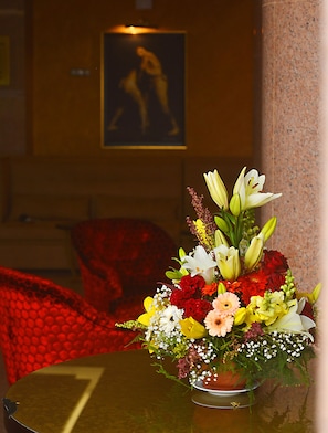Taula amb un arranjament floral en una habitació amb una cadira vermella i un quadre a la paret.