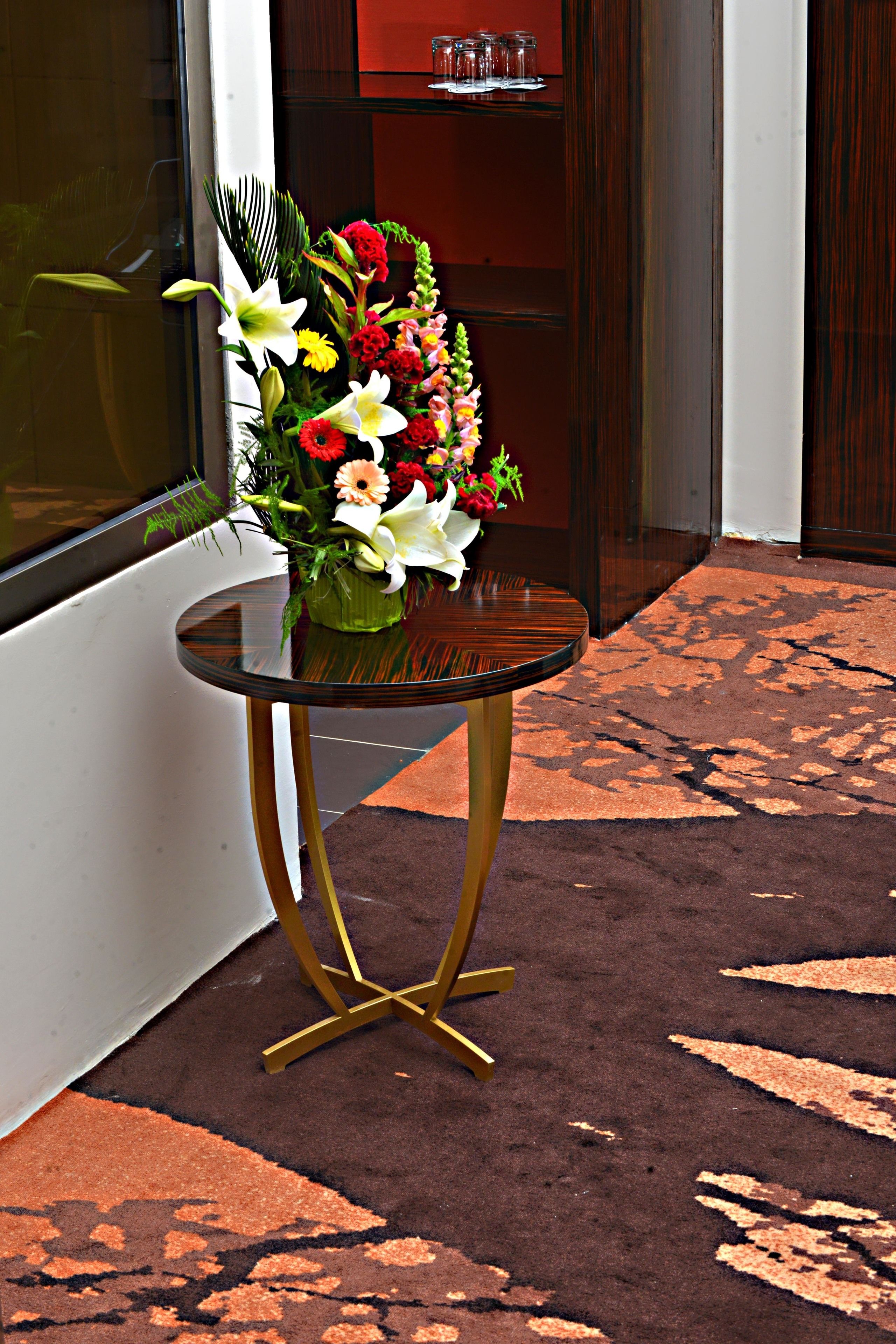 Una mesa de cristal con un arreglo floral en un vestíbulo moderno con alfombra estampada y paneles de madera oscura.