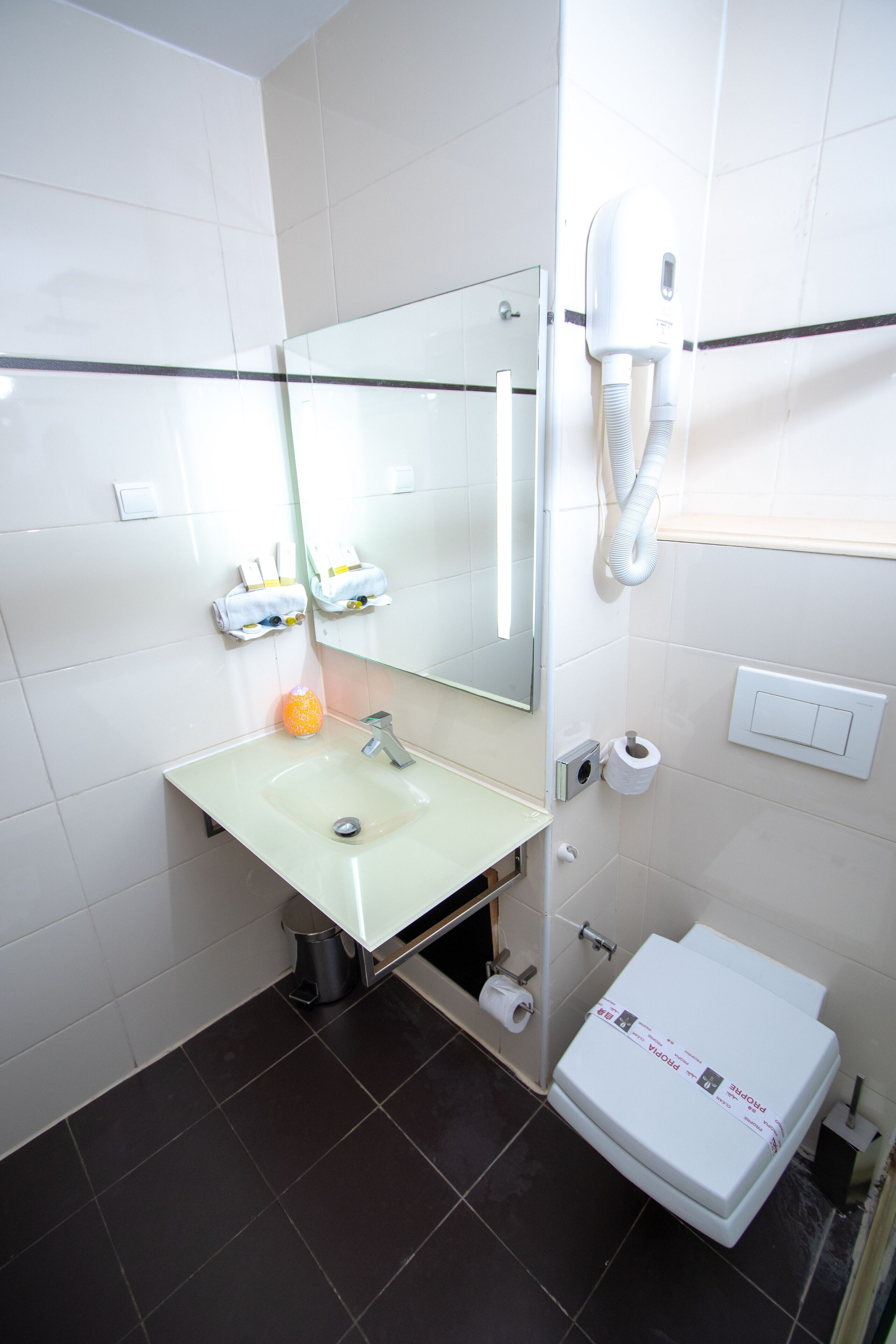 A bathroom with a sink, mirror, toilet, and a hand dryer.