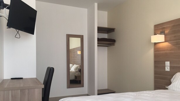 A hotel room with a bed, a desk, a chair, a TV mounted on the wall, a mirror, a bedside table, and a nightstand. - Le Logis Dauphinois (Roussillon-en-Isere)