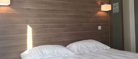 Une chambre à coucher avec une tête de lit en bois, un lit avec une literie blanche et deux lampes fixées au mur.