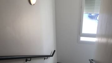 A staircase with a handrail, a light fixture on the wall, and a window with blinds.