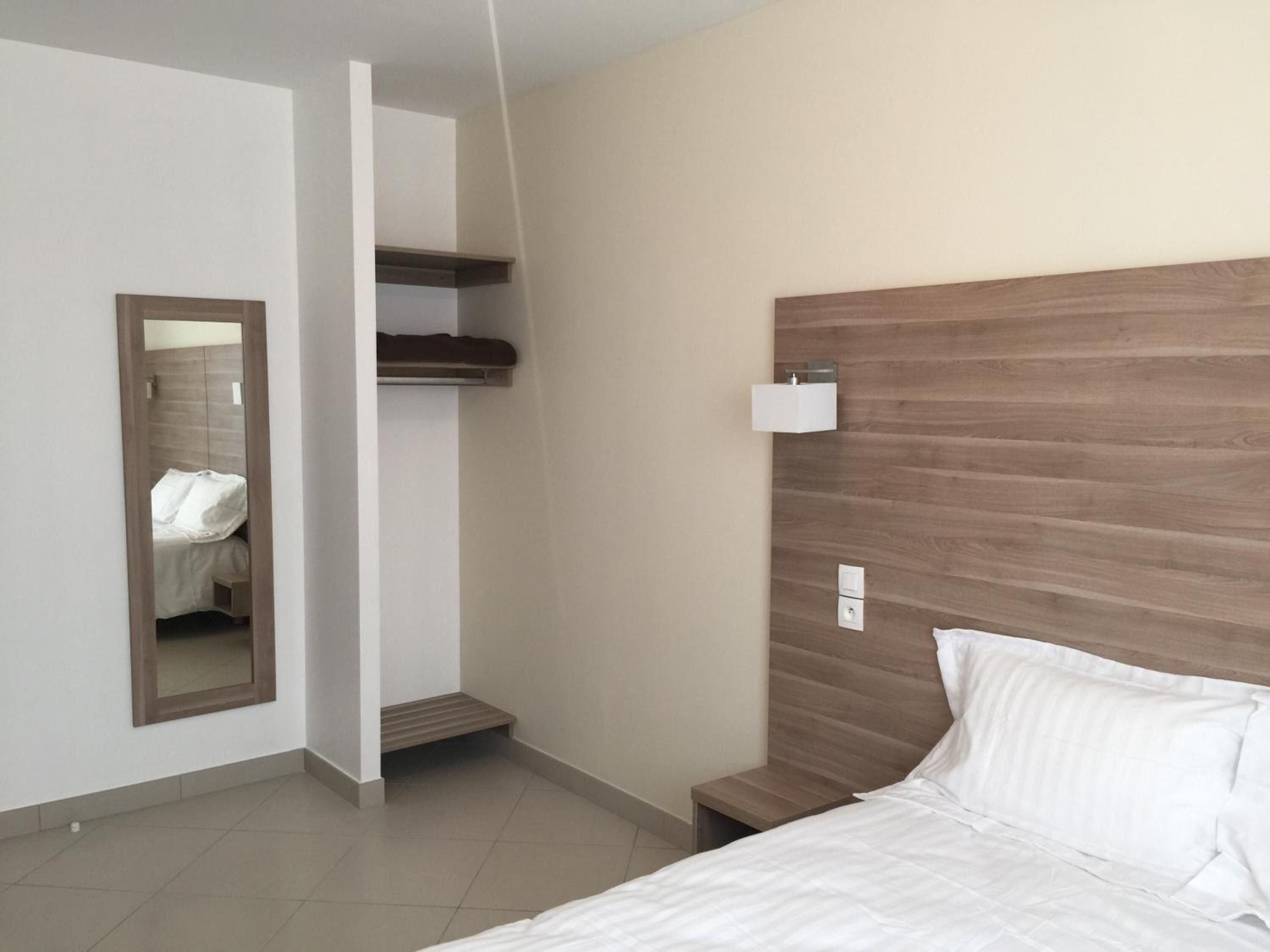 A bedroom with a wooden headboard, a bedside table, a mirror, and a wardrobe.