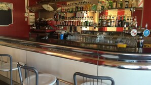 A bar area with a counter, multiple shelves of bottles, and two bar stools. - Le Logis Dauphinois (Roussillon-en-Isere)