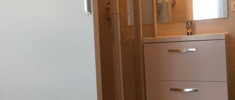 A modern bathroom with a glass shower enclosure, a white vanity with two drawers, and a large mirror above the sink.