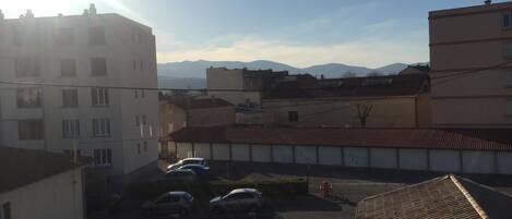 A residential area with buildings, parked cars, and a mountain range in the background.