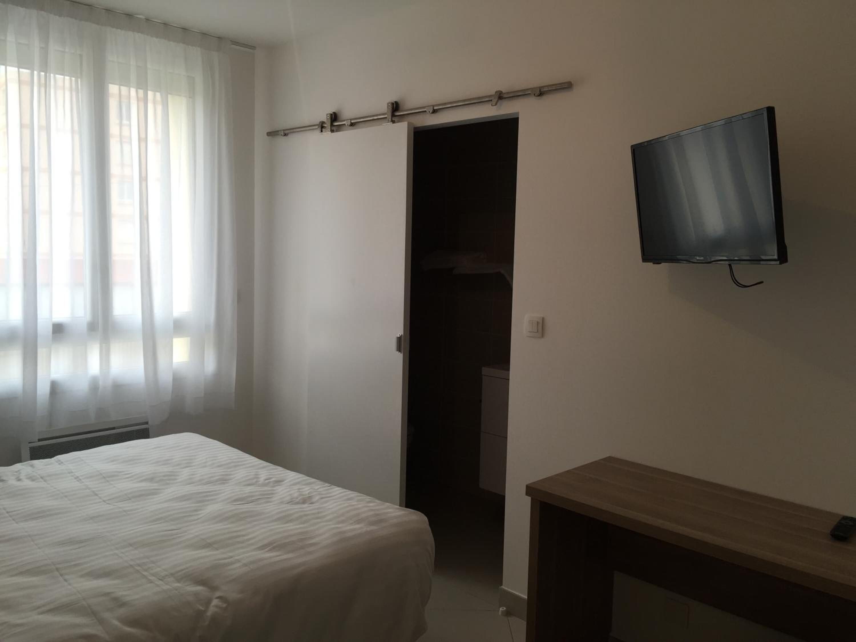 A bedroom with a bed, a TV mounted on the wall, and a wooden bench.