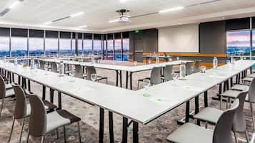 A conference room with long tables, chairs, and a projector screen.