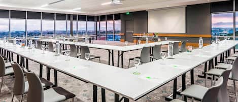 A conference room with long tables, chairs, and a projector screen.