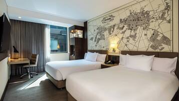 A hotel room with two beds, a desk, a chair, a map on the wall, and a window with curtains.