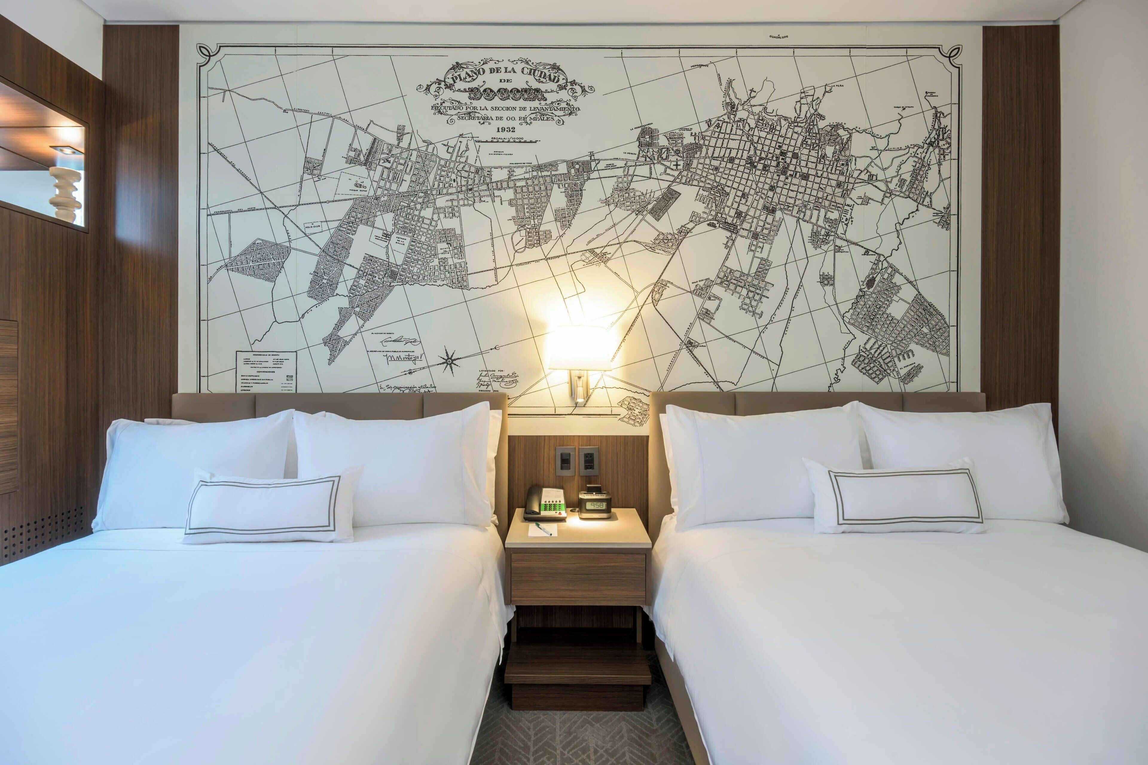 A hotel room with two beds, a nightstand with a lamp, and a large map on the wall.