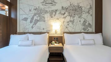 A hotel room with two beds, a nightstand with a lamp, and a large map on the wall.