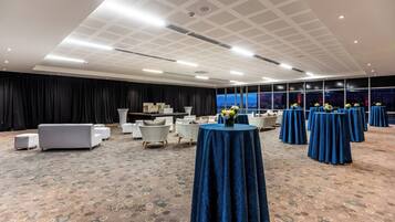 A spacious conference room with a patterned carpet, round tables with blue tablecloths, white sofas, and a black backdrop.