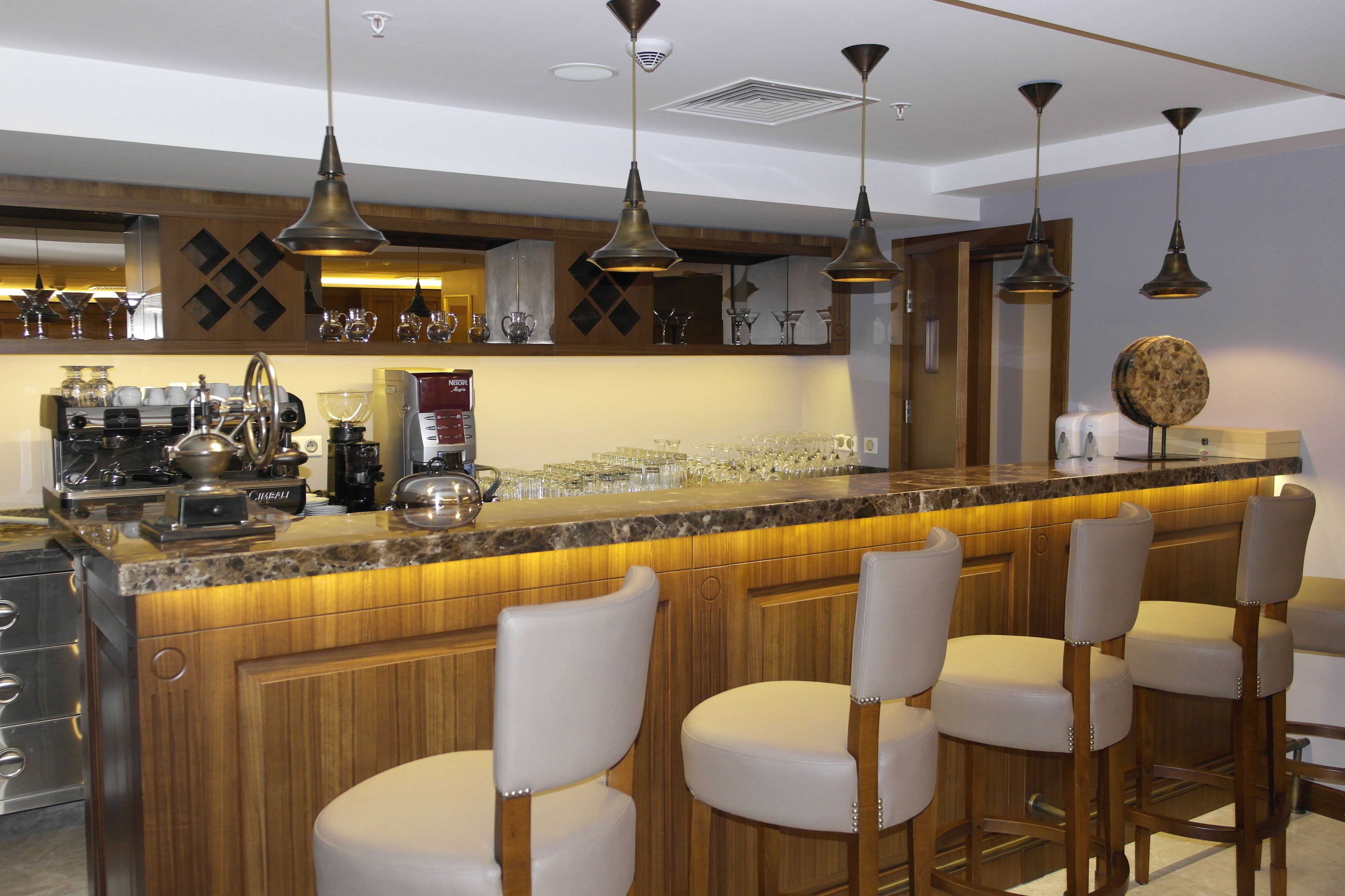 Uma área de bar com armários de madeira, banquetas e luminárias pendentes.