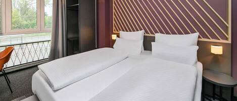 Una habitación de hotel moderna con una cama grande, un escritorio y una silla. Cuenta con una ventana que ofrece vistas a árboles y un balcón.