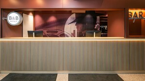 A reception desk with a modern design, a B&B Hotels sign, and a bar area. - B&B HOTEL Berlin-Adlershof (Berlin)