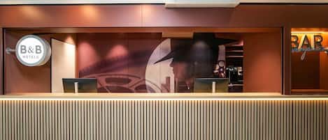 Un comptoir d’accueil au design moderne, une enseigne B&B Hotels et un espace bar.