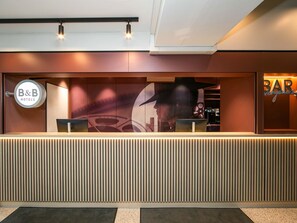 A reception desk with a modern design, a B&B Hotels sign, and a bar area. - B&B HOTEL Berlin-Adlershof (Berlin)