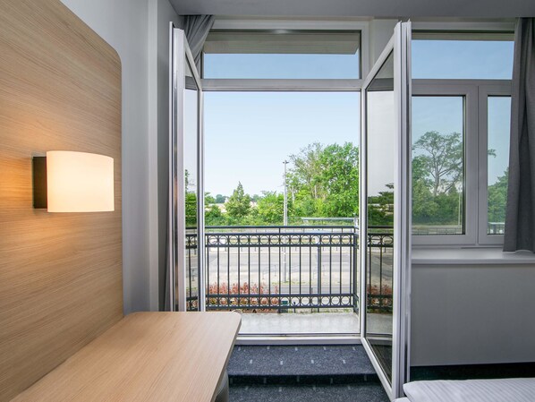 Una moderna camera d'hotel con parete in legno, un comodino, una finestra vista parco e un balcone con ringhiera in metallo.