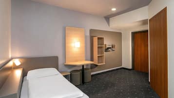 A modern hotel room with a neatly made bed, a bedside table, a wall-mounted shelf with a hanging rack, and a wooden door.