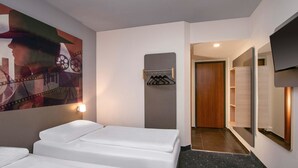 A hotel room with two beds, a wall-mounted TV, a coat rack, and a hallway leading to a bathroom. - B&B HOTEL Berlin-Adlershof (Berlin)