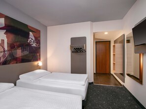 A hotel room with two beds, a wall-mounted TV, a coat rack, and a hallway leading to a bathroom. - B&B HOTEL Berlin-Adlershof (Berlin)