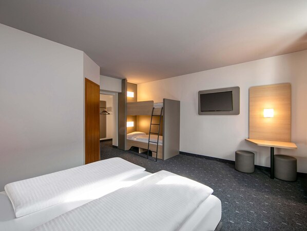 A hotel room with a bed, a desk with a chair, a TV mounted on the wall, and a small table with a lamp. - B&B HOTEL Berlin-Adlershof (Berlin)