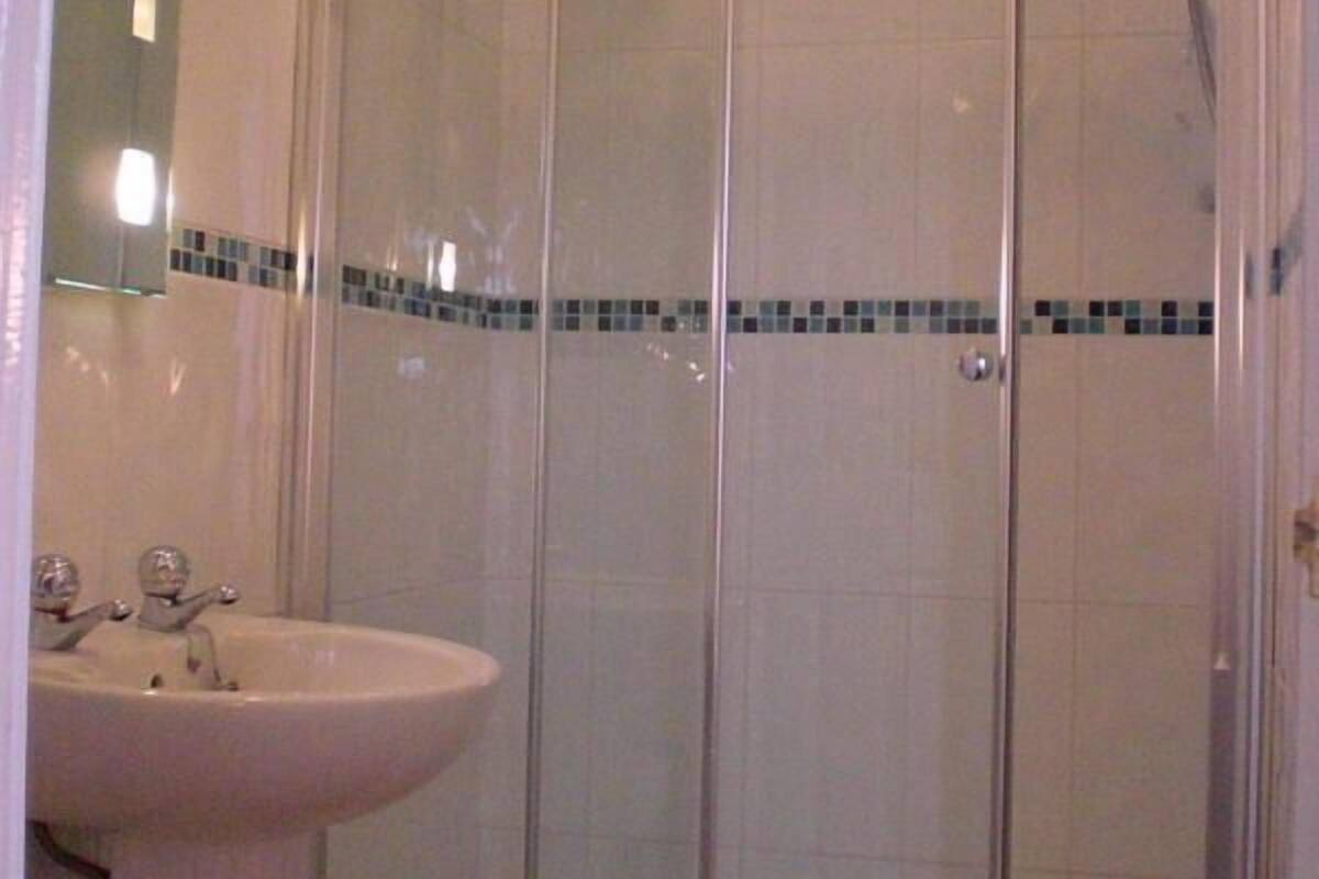 A bathroom with a glass shower enclosure, a sink, and a mirror.