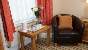 A hotel room with a wooden table, a black leather armchair, a vase with flowers, and a tray with a white pitcher and glasses. - The Old Courthouse (Windermere)