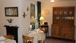A dining area with a table set for two, a wooden cabinet with dishes, and a framed picture on the wall. - The Old Courthouse (Windermere)